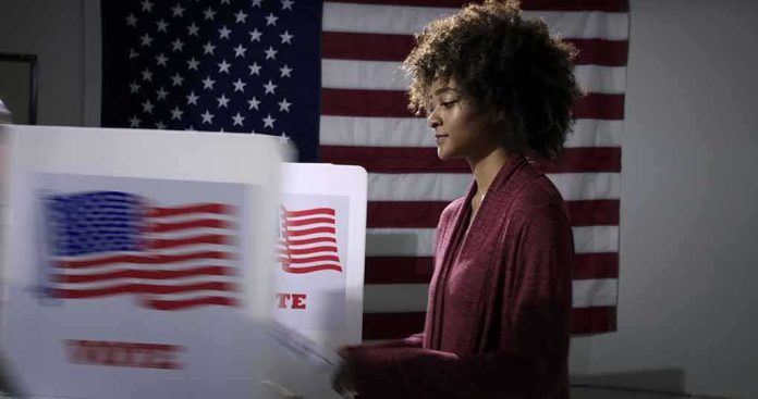 shutterstock_1737374753 Voter at a polling booth with an American flag backdrop