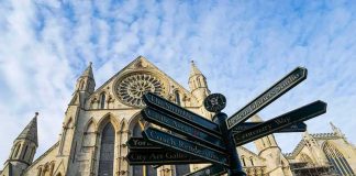 Archbishop Slams ‘Unholy’ Stage Stunt Gothic cathedral with ornate facade and directional signpost in foreground