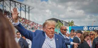 Donald Trump waving while walking through a crowded outdoor event