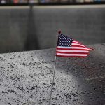 25 Years Later, Americans Say 9/11 Changed Us FOREVER American flag on a rainy memorial nameplate.