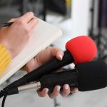 DSA Says It Has Militant Slogans and Nonviolent Strategies Journalist holding two microphones while writing in a notebook