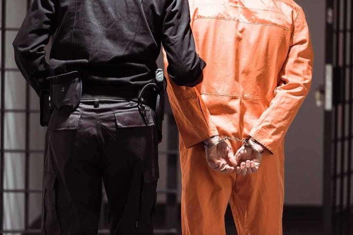 shutterstock_1030213828-1 Prisoner in orange jumpsuit handcuffed with guard standing beside