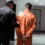 Georgia Killer Gets Execution Date 23 YEARS Later Police officer escorting handcuffed inmate in orange jumpsuit
