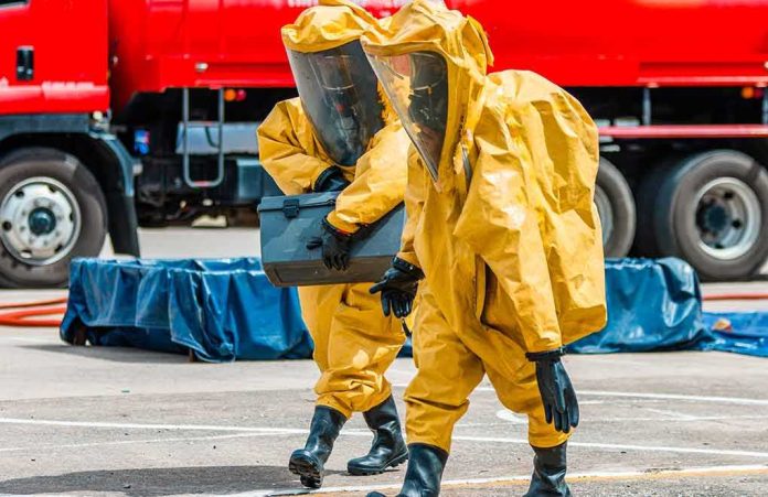 Hazmat workers in yellow suits carry equipment near a tanker truck