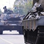 Military tanks drive down a city street