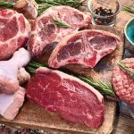 Assorted raw meat cuts with herbs on a wooden board