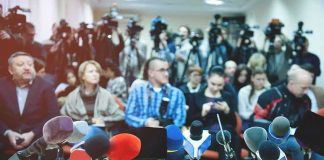 3 Leading News Outlets Say Sudden Banishment Is Unconstitutional Row of microphones at a press conference with audience and cameras behind