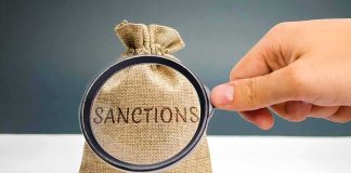 hand holding magnifying glass over burlap money bag with coins