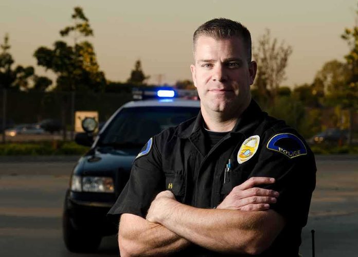 Police officer standing with arms crossed in front of patrol car