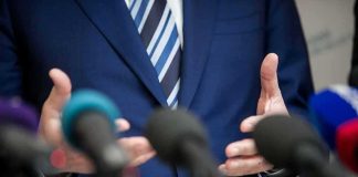 Speaker in blue suit gesturing behind microphones