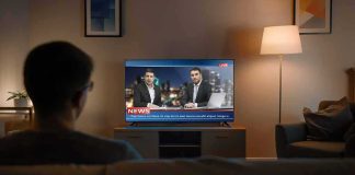 Person watching a live news broadcast on TV in a cozy living room