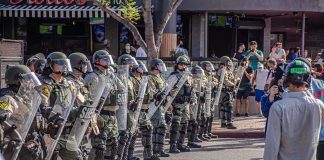 Riot police in helmets and shields form a line on a city street