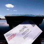 Courts Freeze Trump’s USPS Crackdown Mail-in ballot being inserted into a blue USPS mailbox