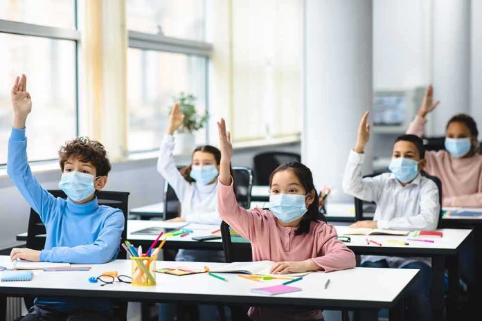 shutterstock_1903224562 Schoolchildren wearing masks raise hands in a classroom