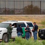 Hispanic Backlash Explodes Over ICE Dragnet law enforcement officers confer beside patrol vehicles near a border fence
