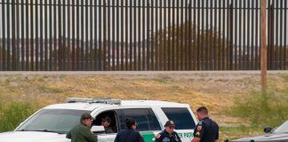 Hispanic Backlash Explodes Over ICE Dragnet law enforcement officers confer beside patrol vehicles near a border fence
