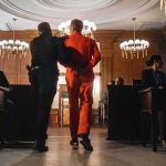 Insanity Defense Drama Collides With Cold Evidence Prisoner in orange jumpsuit escorted by officer in a courtroom