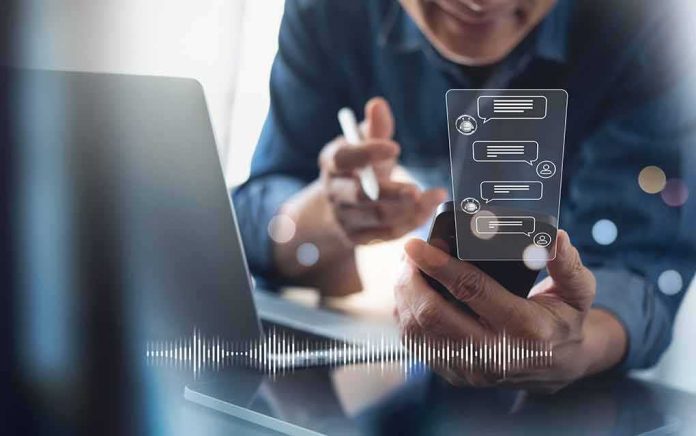 shutterstock_2152122605-1 Person using smartphone with chat bubbles and laptop