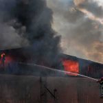 Firefighter on ladder spraying water at warehouse fire