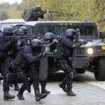 Tactical police team advances from armored vehicle with shields and rifles