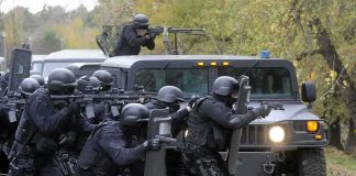 Tactical police team advances from armored vehicle with shields and rifles