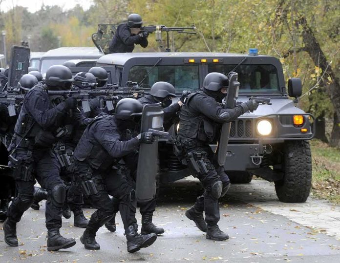 Tactical police team advances from armored vehicle with shields and rifles