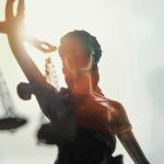 Will WNBA Team Sign Transgender French Basketball Player? Lady Justice statue with scales silhouetted against bright light