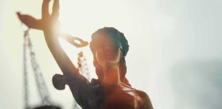 Lady Justice statue with scales silhouetted against bright light