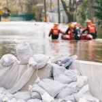 Deadly Floods Turn Entire Towns Into Traps Sandbags stacked near a flooded street with rescue workers in a boat