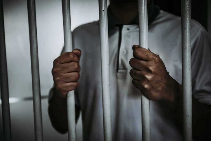 shutterstock_1014307000 Person gripping prison bars with both hands