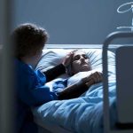 Patient in hospital bed with visitor holding their hand