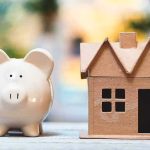 California Home Sales Hit CRISIS Levels Piggy bank beside cardboard house model on a table