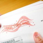Election Offices Targeted by Mystery POWDER A hand holding an envelope labeled Official Election Mail
