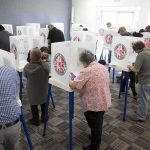 48 Noncitizens Charged With Voting ILLEGALLY Voters fill out ballots at polling booths in a busy voting room