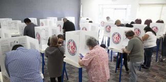 48 Noncitizens Charged With Voting ILLEGALLY Voters fill out ballots at polling booths in a busy voting room