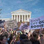 Protesters with signs in front of a neoclassical courthouse