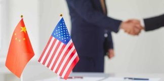 Chinese and American flags on a table with a handshake in the background