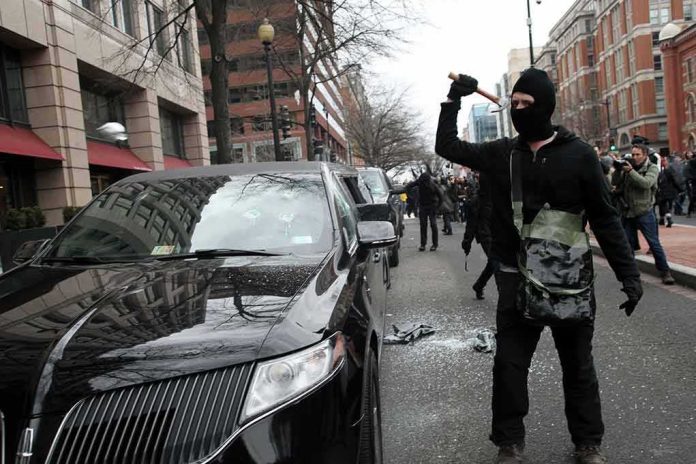 shutterstock_679827301 Masked protester raises tool to strike black car on city street