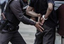 Police arresting person against a wall outdoors