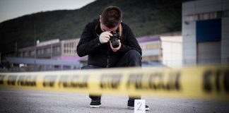Person photographing crime scene evidence behind police tape