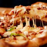 Cheesy pizza slice being lifted from whole pizza
