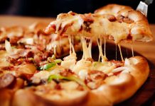 Cheesy pizza slice being lifted from whole pizza