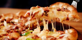 Cheesy pizza slice being lifted from whole pizza