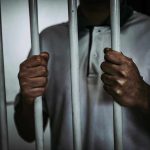 Person holding jail cell bars tightly