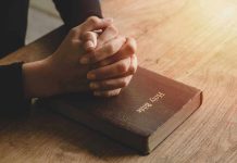 Hands praying on a Bible