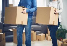 Two people carrying cardboard boxes indoors.