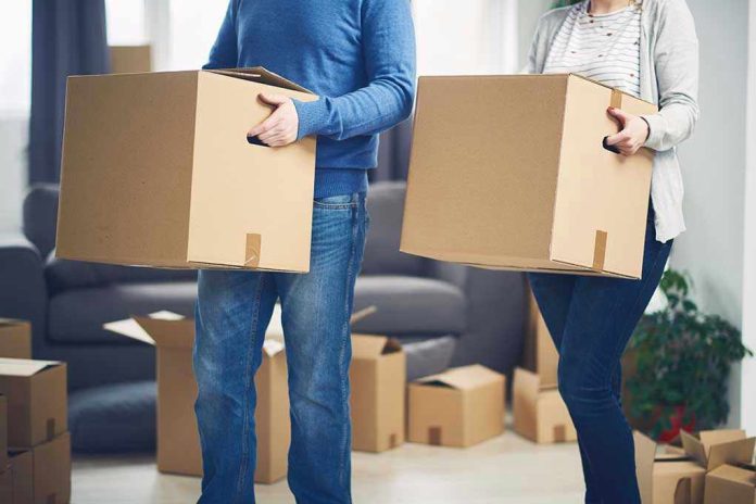 567850450 Two people carrying cardboard boxes indoors.