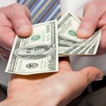 Two hands exchanging cash bills in a business context