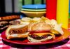 A plate with a hamburger, hot dog, and potato chips on a picnic table