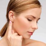 Profile view of a woman gently touching her ear with a thoughtful expression